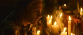 Movie still from “The Mother” (2023), directed by Niki Caro – A man stares into the distance in front of candles; Close Up shot, Over the shoulder angle