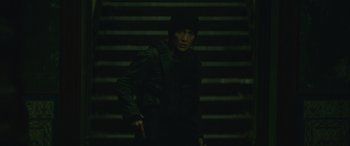 Movie still from “The Mother” (2023), directed by Niki Caro – A man standing in front of some steps at night; Medium shot, High angle