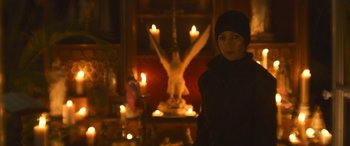 Movie still from “The Mother” (2023), directed by Niki Caro – A woman standing in front of a statue of an angel; Medium shot, Low angle