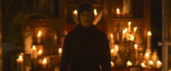 Movie still from “The Mother” (2023), directed by Niki Caro – A woman standing in front of candles in a room; Medium shot, Low angle