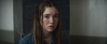 Movie still from “The Mother” (2023), directed by Niki Caro – A young girl with long hair is looking at the camera; Close Up shot, Over the shoulder angle