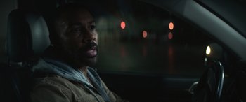Movie still from “The Mother” (2023), directed by Niki Caro – A man sitting in the back seat of a car at night; Close Up shot, Over the shoulder angle