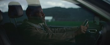 Movie still from “The Mother” (2023), directed by Niki Caro – A man sitting in the drivers seat of a car; Close Up shot, Low angle