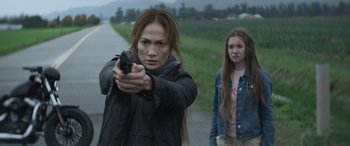 Movie still from “The Mother” (2023), directed by Niki Caro – A woman holding a gun while standing next to a young girl; Close Up shot, Over the shoulder angle