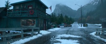 Movie still from “The Mother” (2023), directed by Niki Caro – A snowy street with a mountain in the background; Extreme Wide shot, High angle