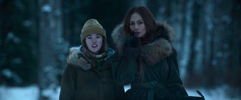 Movie still from “The Mother” (2023), directed by Niki Caro – Two young women standing next to each other in winter clothing; Medium shot, Low angle
