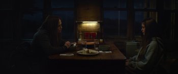 Movie still from “The Mother” (2023), directed by Niki Caro – A woman sitting at a table with a plate of food; Medium shot, Over the shoulder angle
