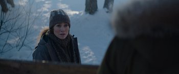 Movie still from “The Mother” (2023), directed by Niki Caro – A woman wearing a hat and scarf in the snow; Medium shot, Over the shoulder angle