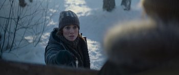 Movie still from “The Mother” (2023), directed by Niki Caro – A woman wearing a winter hat and a scarf; Medium shot, Over the shoulder angle