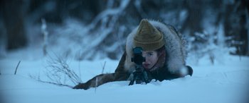 Movie still from “The Mother” (2023), directed by Niki Caro – A person in the snow taking a picture with a camera; Medium shot, Low angle