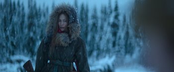 Movie still from “The Mother” (2023), directed by Niki Caro – A woman in a fur trimmed coat standing in the snow; Medium shot, Over the shoulder angle