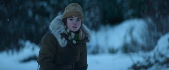 Movie still from “The Mother” (2023), directed by Niki Caro – A young girl wearing a winter coat and a hat; Close Up shot, Low angle