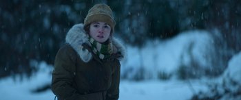 Movie still from “The Mother” (2023), directed by Niki Caro – A young girl in a brown coat and a yellow hat; Close Up shot, Over the shoulder angle