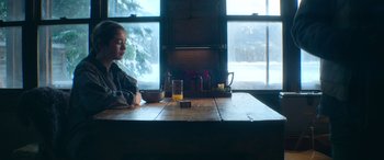 Movie still from “The Mother” (2023), directed by Niki Caro – A child sitting at a table with a glass of beer; Wide shot, Over the shoulder angle
