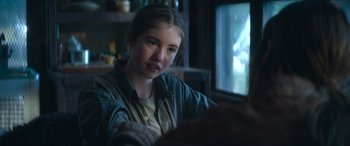 Movie still from “The Mother” (2023), directed by Niki Caro – A young girl sitting in front of a television; Close Up shot, Over the shoulder angle
