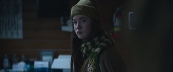Movie still from “The Mother” (2023), directed by Niki Caro – A young girl wearing a hat and a scarf; Close Up shot, Over the shoulder angle