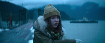 Movie still from “The Mother” (2023), directed by Niki Caro – A young girl wearing a winter coat and a hat; Close Up shot, Over the shoulder angle