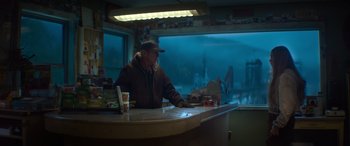 Movie still from “The Mother” (2023), directed by Niki Caro – A man sitting at a counter in a restaurant; Wide shot, Low angle