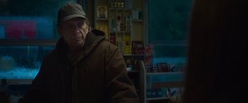 Movie still from “The Mother” (2023), directed by Niki Caro – An older man wearing a brown jacket and a hat; Medium shot, Over the shoulder angle