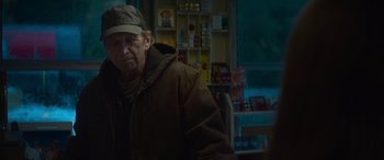 Movie still from “The Mother” (2023), directed by Niki Caro – An older man wearing a hat and a jacket; Medium shot, Over the shoulder angle