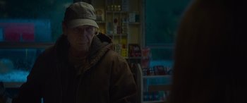 Movie still from “The Mother” (2023), directed by Niki Caro – An older man wearing a hat and a jacket; Close Up shot, Over the shoulder angle