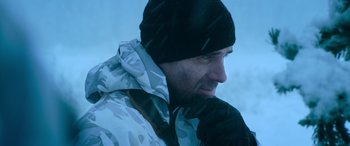 Movie still from “The Mother” (2023), directed by Niki Caro – A person wearing a jacket and a hat; Close Up shot, Low angle