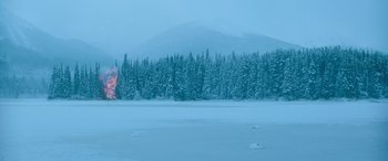 Movie still from “The Mother” (2023), directed by Niki Caro – A fire is burning in the middle of a snowy forest; Extreme Wide shot, High angle