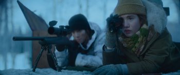 Movie still from “The Mother” (2023), directed by Niki Caro – Two people are laying in the snow looking through binoculars; Medium shot, Over the shoulder angle