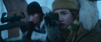 Movie still from “The Mother” (2023), directed by Niki Caro – A young girl wearing a winter hat and gloves holding a camera; Close Up shot, Over the shoulder angle