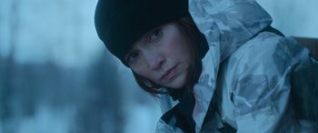 Movie still from “The Mother” (2023), directed by Niki Caro – A person wearing a jacket and a hat; Close Up shot, Low angle