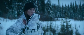 Movie still from “The Mother” (2023), directed by Niki Caro – A woman wearing a camouflage jacket in the snow; Medium shot, Over the shoulder angle