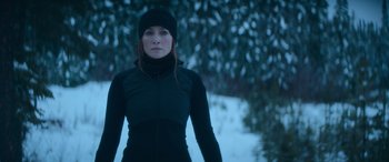 Movie still from “The Mother” (2023), directed by Niki Caro – A woman in a black jacket and a black hat is standing in the snow; Medium shot, Low angle
