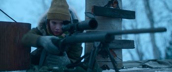 Movie still from “The Mother” (2023), directed by Niki Caro – A young boy is holding a rifle and aiming it; Medium shot, Low angle