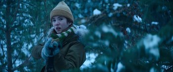 Movie still from “The Mother” (2023), directed by Niki Caro – A young boy in a winter coat and hat is playing with a toy gun; Medium shot, Over the shoulder angle