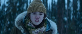 Movie still from “The Mother” (2023), directed by Niki Caro – A young girl wearing a winter coat and a hat; Close Up shot, Low angle