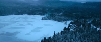 Movie still from “The Mother” (2023), directed by Niki Caro – A view of a frozen lake with a lot of trees in the background; Extreme Wide shot, High angle