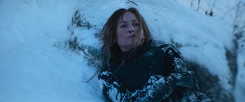 Movie still from “The Mother” (2023), directed by Niki Caro – A woman laying in the middle of a snow covered field; Close Up shot, High angle