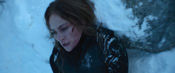 Movie still from “The Mother” (2023), directed by Niki Caro – A young woman laying on the ground in the snow; Close Up shot, Overhead angle