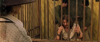 Movie still from “The Mummy” (1999), directed by Stephen Sommers – A man sitting in a jail cell behind bars with another man standing behind him; Medium shot, Over the shoulder angle