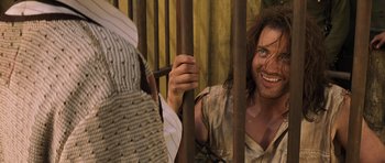 Movie still from “The Mummy” (1999), directed by Stephen Sommers – A man holding onto a metal bar while another man looks on; Medium shot, Over the shoulder angle