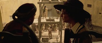 Movie still from “The Mummy” (1999), directed by Stephen Sommers – Two people in a courtyard looking at a crowd of people; Medium shot, Over the shoulder angle