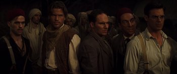 Movie still from “The Mummy” (1999), directed by Stephen Sommers – A group of men standing next to each other in a dark room; Medium shot, Over the shoulder angle