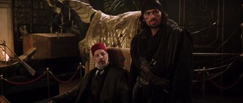 Movie still from “The Mummy” (1999), directed by Stephen Sommers – Two men dressed in medieval costumes sitting in a chair; Medium shot, Over the shoulder angle