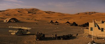 Movie still from “The Mummy” (1999), directed by Stephen Sommers – A group of people sitting in the sand near some tents; Extreme Wide shot, High angle