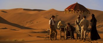 A man standing in the desert next to an old gramophone