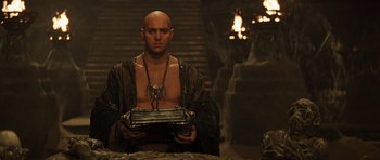 Movie still from “The Mummy” (1999), directed by Stephen Sommers – A bald man holding a tray in a dark room; Medium shot, Low angle