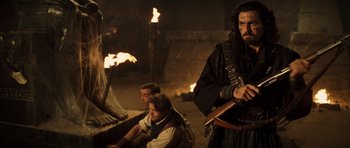 Movie still from “The Mummy” (1999), directed by Stephen Sommers – A group of people sitting around a fire pit; Medium shot, Over the shoulder angle