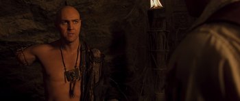 Movie still from “The Mummy” (1999), directed by Stephen Sommers – A man with a bare chested standing next to a lamp; Medium shot, Over the shoulder angle