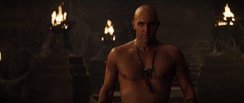 Movie still from “The Mummy” (1999), directed by Stephen Sommers – A man with a bare chest is standing in front of a fire; Medium shot, Low angle