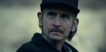Movie still from “Dopesick” (2021), directed by Danny Strong – An older man with a beard and mustache wearing a hat; Close Up shot, Over the shoulder angle